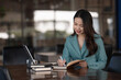 © Songsak C - Businesswoman writing a note while using laptop at a table in an office.