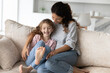 Overjoyed cute little girl with mother engaged in funny activity, cuddling and tickling sitting on couch at home, excited mom with adorable daughter having fun together, enjoying leisure time