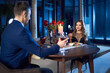© serhiibobyk - Side view of beautiful young woman and young handsome man in elegant suit with red wine glasses dating and toasting in restaurant. Concept of romantic supper in restaurant.