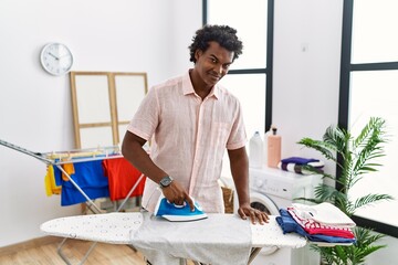 Poster - African man with curly hair ironing clothes at home with a happy and cool smile on face. lucky person.