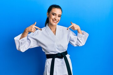 Wall Mural - Beautiful brunette young woman wearing karate fighter uniform with black belt looking confident with smile on face, pointing oneself with fingers proud and happy.