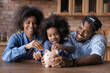 © fizkes - Caring young African American couple parents teaching small biracial kid daughter saving money, planning future purchases together, putting coins in small piggybank, financial education for children.