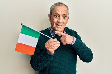 Wall Mural - Handsome senior man with grey hair holding ireland flag smiling happy pointing with hand and finger