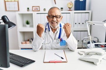 Wall Mural - Mature doctor man at the clinic excited for success with arms raised and eyes closed celebrating victory smiling. winner concept.