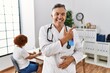 © Krakenimages.com - Middle age doctor man at the clinic with a patient cheerful with a smile of face pointing with hand and finger up to the side with happy and natural expression on face