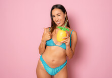 Beautiful Smiling Woman In Bikini Drinking Juice Isolated Over Pink Background.