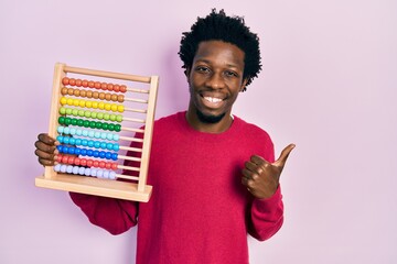 Young african american man holding traditional abacus smiling happy and positive, thumb up doing excellent and approval sign