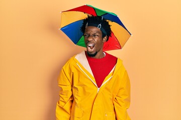 Poster - Young african american man wearing yellow raincoat angry and mad screaming frustrated and furious, shouting with anger. rage and aggressive concept.