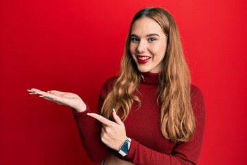 Sticker - Young blonde woman wearing turtleneck sweater amazed and smiling to the camera while presenting with hand and pointing with finger.