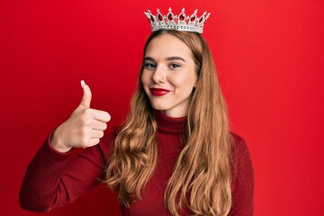 Canvas Print - Young blonde woman wearing princess crown smiling happy and positive, thumb up doing excellent and approval sign