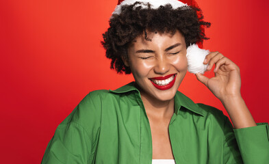 Wall Mural - New Year and women beauty. Happy african american girl celebrates christmas, wearing santa hat and smiling, laughing carefree, standing over red background