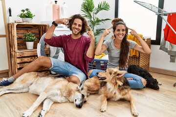 Sticker - Young hispanic couple doing laundry with dogs smiling pointing to head with both hands finger, great idea or thought, good memory