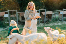Happy Smiling Woman And Little Girl Feed Goats On The Farm. Agritourism In The Countryside.