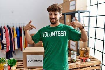 Poster - Young arab man wearing volunteer t shirt at donations stand looking confident with smile on face, pointing oneself with fingers proud and happy.