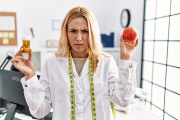 Sticker - Beautiful blonde nutritionist woman holding fat pills skeptic and nervous, frowning upset because of problem. negative person.