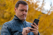 © sommersby - Sad millennial guy looks at phone screen in surprise and stands outside at autumn. Disgusted and overwhelmed young man stares at screen of smart phone, needs to pay debts immediately