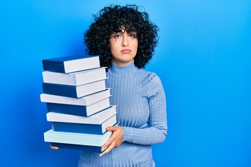 Poster - Young middle east woman holding a pile of books relaxed with serious expression on face. simple and natural looking at the camera.