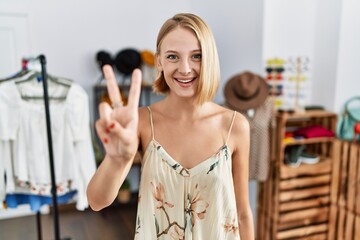 Poster - Young caucasian woman at retail shop showing and pointing up with fingers number two while smiling confident and happy.