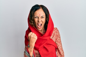 Poster - Middle age hispanic woman wearing tradition sherwani saree clothes angry and mad raising fist frustrated and furious while shouting with anger. rage and aggressive concept.