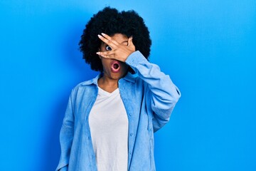 Canvas Print - Young african american woman wearing casual clothes peeking in shock covering face and eyes with hand, looking through fingers with embarrassed expression.