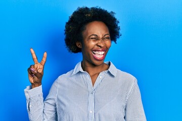 Wall Mural - Young african american woman wearing casual clothes smiling with happy face winking at the camera doing victory sign. number two.