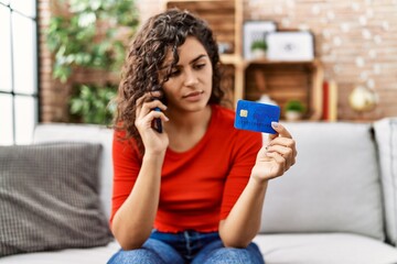 Poster - Young latin woman talking on the smartphone using credit card and laptop at home