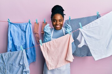 Wall Mural - African american woman with braided hair washing clothes at clothesline doing money gesture with hands, asking for salary payment, millionaire business