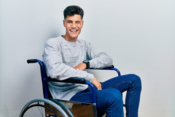 Poster - Young hispanic man sitting on wheelchair winking looking at the camera with sexy expression, cheerful and happy face.