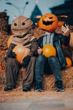 A Guy With A Pumpkin Head Sits Next To A Scarecrow