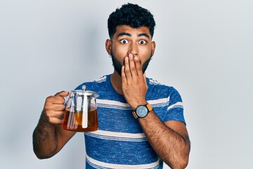 Poster - Arab man with beard holding traditional tea pot covering mouth with hand, shocked and afraid for mistake. surprised expression