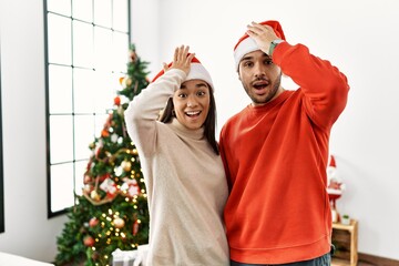 Poster - Young hispanic couple standing by christmas tree surprised with hand on head for mistake, remember error. forgot, bad memory concept.