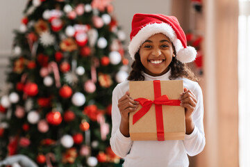 Wall Mural - Black Girl In Santa Hat Holding Christmas Present At Home