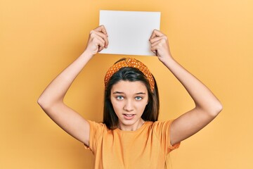 Poster - Young brunette girl holding blank empty banner over head clueless and confused expression. doubt concept.