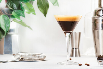 Espresso martini, trendy alcoholic cocktail with vodka, coffee liqueur, syrup and ice, black background, bar tools