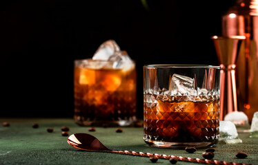 Black russian cocktail, trendy alcoholic drink with vodka, coffee liqueur and ice, rusty green dark background, bar tools