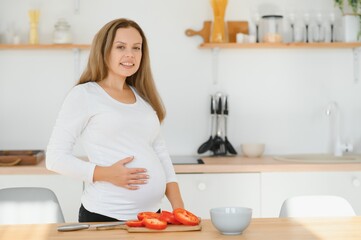 Wall Mural - pregnant woman slicing vegetables at home in the kitchen