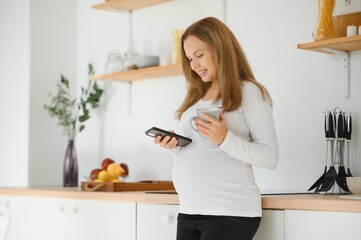 Wall Mural - Beautiful pregnant woman drinks tea or coffee. Indoor photo.