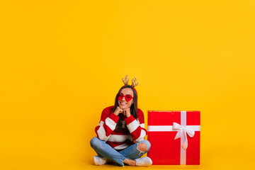 Wall Mural - Full length photo of happy young smiling beautiful and charming woman in Christmas reindeer antlers while she sitting with big red gift box