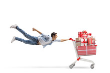 Full Length Shot Of A Casual Young Man Flying And Holding A Shopping Cart With Christmas Presents