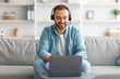 © Prostock-studio - Smiling young Caucasian guy in headset making video call on laptop at home, talking to webcam
