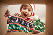 © Iryna Dincer - Happy surprised Caucasian little boy in Santa's hat looking inside a cardboard box, at home near Christmas tree, bottom view. Excited little kid opening Christmas present.