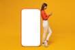 © Damir Khabirov - Young woman standing near huge phone mock up for app, isolated on yellow background