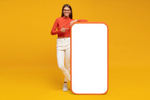 Young Woman Standing And Showing With Finger Blank Screen Of Huge Phone, Mockup For Your App