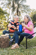 © ADDICTIVE STOCK - Smiling elderly spouses sharing smartphone and having picnic in nature