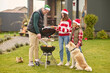 © zinkevych - A cute girl in na santa hat standing the outdors grill while her father cooking