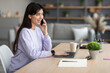 © Prostock-studio - Smiling woman working and talking on cellphone at home