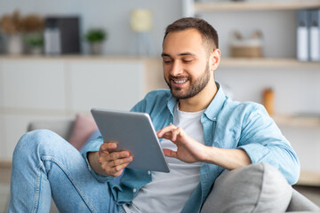 Poster - Cheerful young man using tablet pc, working or studying online from home