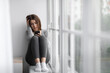 Leinwandbild Motiv Despaired upset millennial millennial woman sitting on windowsill at home and reading message on phone, cry alone