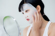 © N_studio - Beautiful young asian woman with sheet facial mask and looking mirror at home, beauty girl applying cosmetic and makeup and touch face with skin care for wrinkle, skincare treatment and moisturizer.