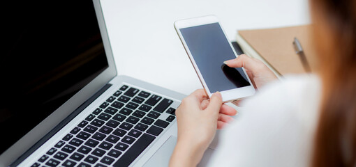 Wall Mural - hand of young woman working with laptop computer and smartphone mockup on desk at home, notebook and